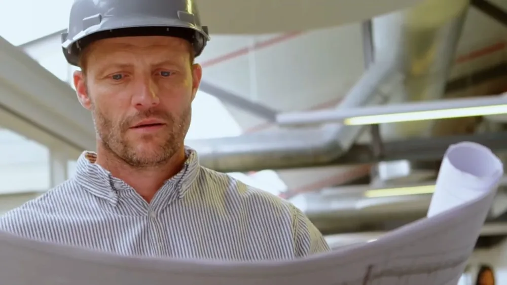 Man in a hard hat studying a set of rolled plumbing plans